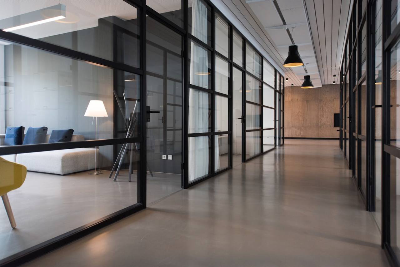 A quiet, modern office corridor lined with glass meeting rooms