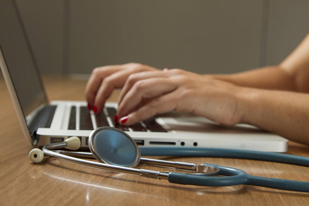 A stethoscope resting beside a laptop in a clinical office